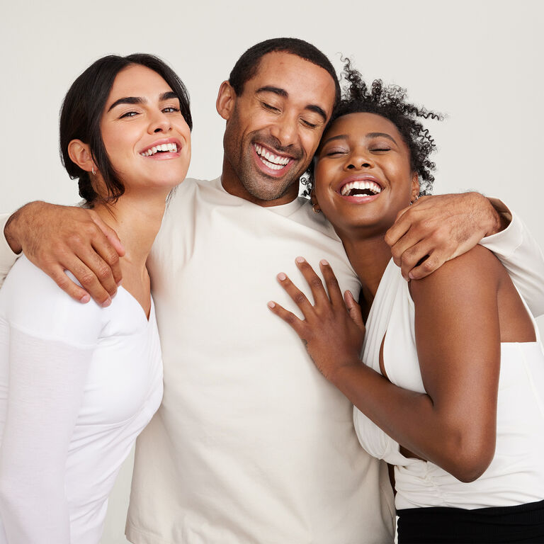 A group of two women and one man hugging and laughing